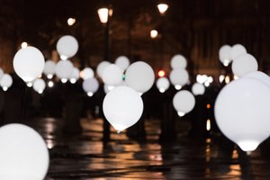 Many balloons float above a dark street - the balloons are lit like light bulbs.
