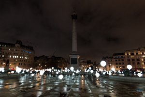 Many balloons float above the ground of Trafalgar Square - the balloons are lit like light bulbs.
