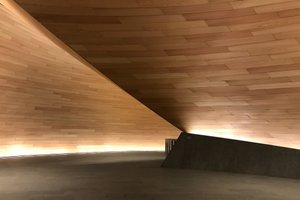 The entrance to the Bloomberg building. There are sweeping wooden walls leading to another room.