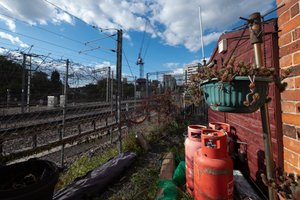 A photo along some railwaylines. There’s train tracks on the left and three red gas canisters on the right.