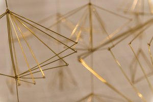 A closeup of a sculpture made from gold-coloured wires bent in to angled shapes.