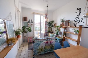 A wide-angle photo of a living room. It’s very bright, with wooden furniture and floral patterns.