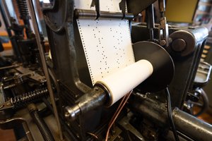 Macro photo of a roll of paper with small holes punched out of it. The roll is being fed through some machinery.