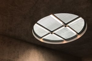 A circular skylight. The surrounding ceiling and walls are dark concrete.