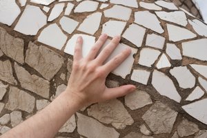 A hand rests on a large mosaic of broken white tiles.