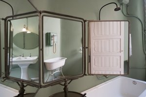 A photo of a 3-part folding mirror in a bathroom. Reflected in the mirrors are a sink, a bath, and a doorway.
