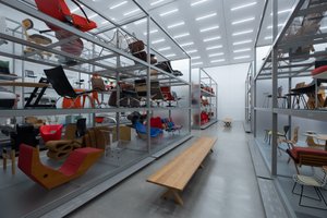 Inside the Vitra Design Museum archive. The room is brightly lit with aluminium shelves on each side receding in to the distance. On the shelves are many different chairs.
