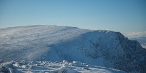 Looking across the edge of a snowy mountain. There’s tiny specks from walkers on the hills