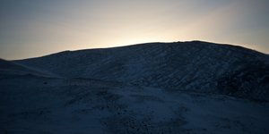 A panorama of a snowy hillside as the sun has set behind the hill.