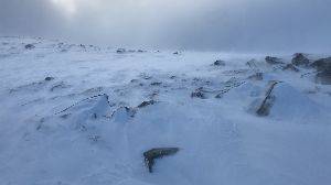 A video of a windswept snowy hill. There’s strong wind blowing towards the camera carrying snow flurries.