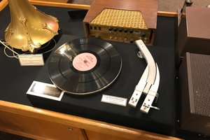 A photograph of a vintage radio player. The player has two reading heads side by side rather than one. The record has two visible tracks.