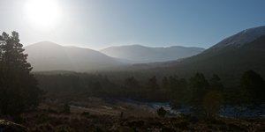 A sunny valley early in the morning. There’s a bit of mist in the background and several layers of mountains visible.