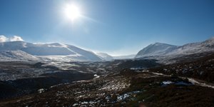 A wide panorama of the Gleann Eanaich valley. There’s snow on the upper parts of the mountains and in the valley it’s mostly brown.