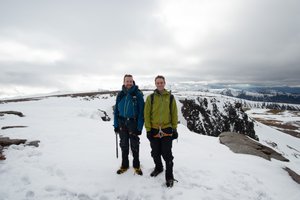 Chris and Ed stand at the top of Fiacaill ridge. The ground is mostly snowy with patches of brown.