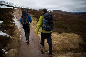 Chris and our instructor walk along a path uphill. There’s small patches of snow in the distance, but the ground is otherwise brown and windswept.