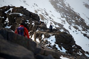 A photo taken facing along Fiacaill ridge. There’s climbers walking along various sections of it, with one in the foreground.