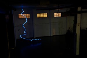 A photo taken in a dark warehouse from above, looking down. There’s a single blue line of light snaking from the floor to the ceiling.