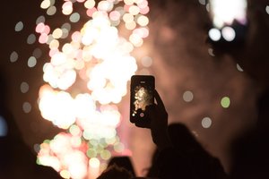 A phone is held taking a photo of fireworks in the distance.