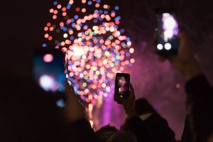 Three phones are held in the air taking photos of fireworks in the distance.