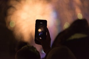 A phone is held taking a photo of fireworks in the distance.