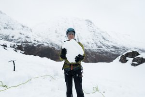 Chris holds a large boulder of snow as he faces the camera.