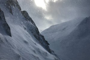 A snowy mountainside and valley, with swirls of snow in the air.