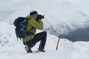 Chris kneeling on a snowy plateau taking a photo.