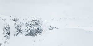 A long telephoto photo of a snowy ridge in the distance. A few small brightly coloured figures can be seen on the ridge.