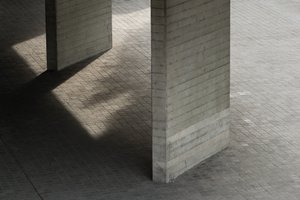 Looking down on two concrete supports for the first floor terrace of the National Theatre. The floor is tiled and the photo is otherwise very grey.
