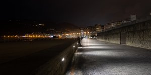 At night time, looking down the beach promenade to the city. There’s a mix of yellow sodium lamps with more modern white leds.