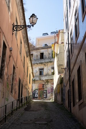 Looking up an alleyway. The foreground is dark and in shadow, but the background is brightly lit by sun. The alley ends with a light coloured building covered in graffiti.
