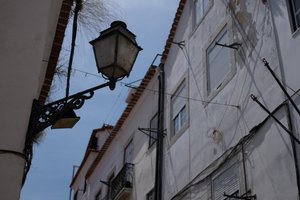Looking up at a streetlamp in a narrow street. It’s daylight, so the streetlamp isn’t on.
