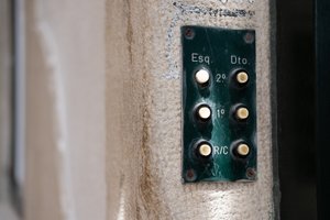 A macro photo of a set of doorbells on the wall. There are 6 white buttons on a dark green base.