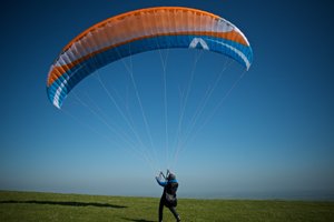 A paraglider stands on the ground with a large sail inflated overhead.