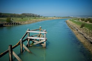 Looking down a greenish-blue river, with rotting wooden posts in the foreground.