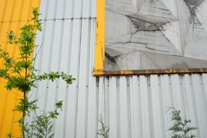 A close shot of the wall of the Rezola cement factory. The wall is made of grey corrugated steel with yellow trim.