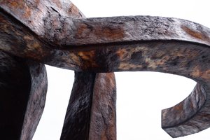 A close photo of a rusting iron sculpture by artist Eduardo Chillida. The sculpture splits in to three arms that curve outwards and then inwards.
