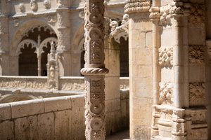 An exterior view of the internal courtyard in the Jerónimos monastery. Several decorative carved pillars in light sandy stone can be seen in strong sunlight.