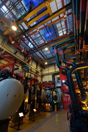 An interior photo of some boilers in Maat. The room is filled with pipes of all sizes and is generally painted in bright primary colours.