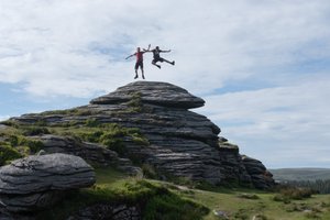 Two people at the top of a tor are jumping in the air.