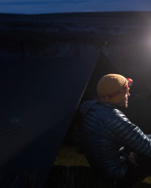 Ed Horsford sat on the ground near a tarp looking away from the camera. He’s lit from one side.