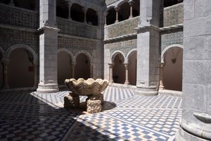 A view of the open-air courtyard in the centre of Pena Palace. The courtyard has blue and white checkerboard tiles, and a large fountain in the shape of a shell in the center.