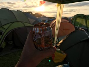 Holding a Beavertown beer can in golden sunset by a group of tents.