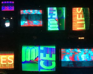Several vintage TVs stacked together display abstract brightly coloured slogans.