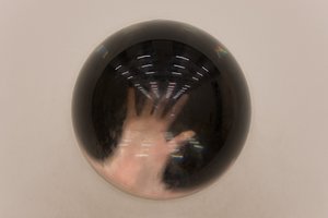 A semicircle of solid glass sits in a white wall. A hand is visible on the other side, magnified.