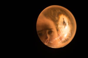 A solid sphere of glass fills the right frame of the photo, set against black. There’s an image of a woman’s face magnified inside the glass.