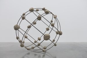 A sphere is formed by several large rings of steel intersecting each other. At each intersection is a clump of rough concrete.