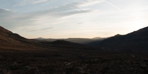 A photo of a valley in Torridon, just before sunrise. The sky is bright, but the land very dark still.