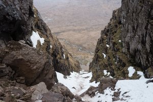 Looking down a steep gully from up high. The base of the gully is filled with snow.