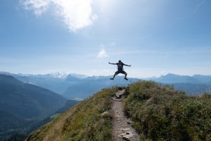 Oj in the air, mid jump. He’s high up on a mountainside in the bright sun.